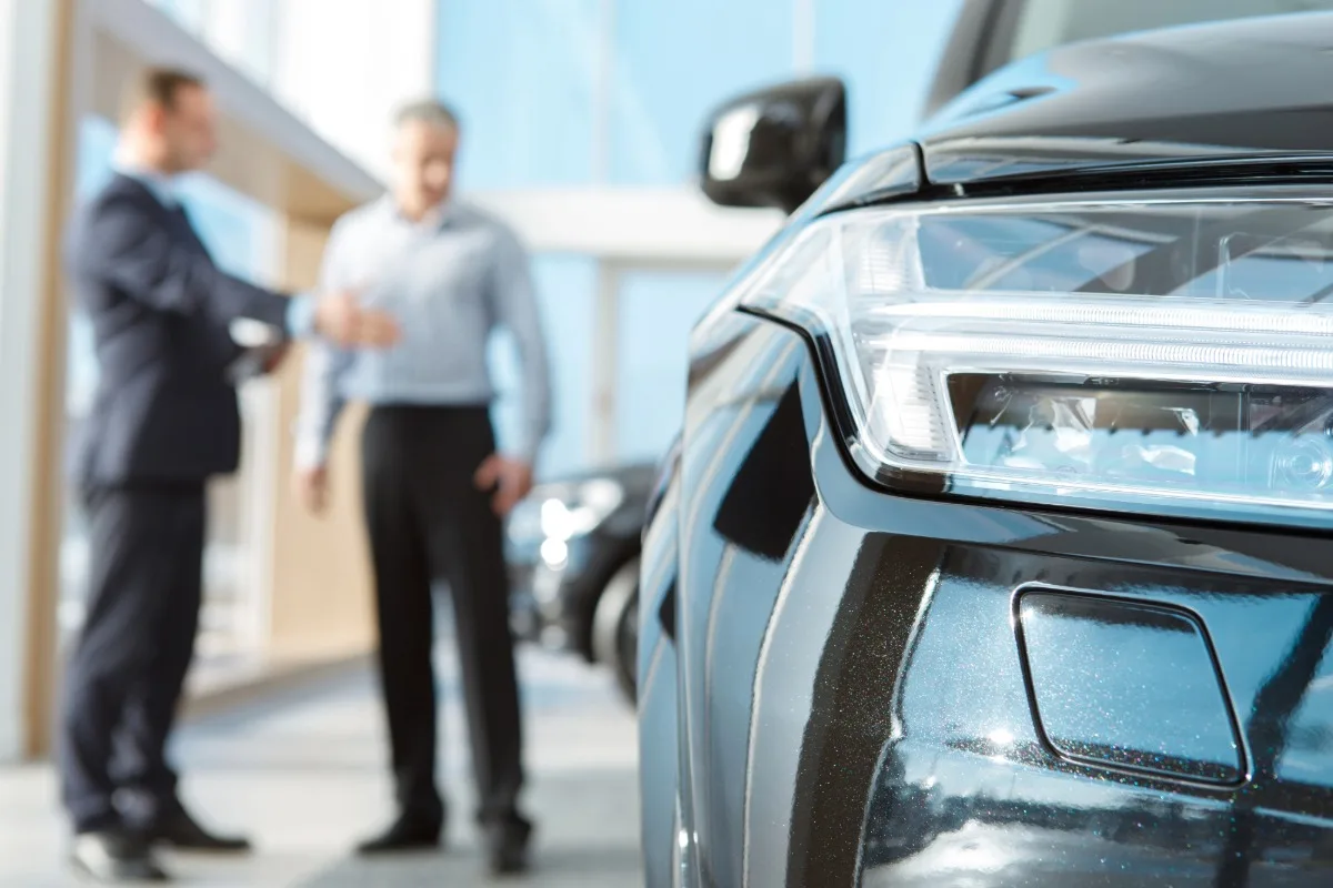 Zwei Personen im Hintergrund, im Vordergrund Ausschnitt eines Autos